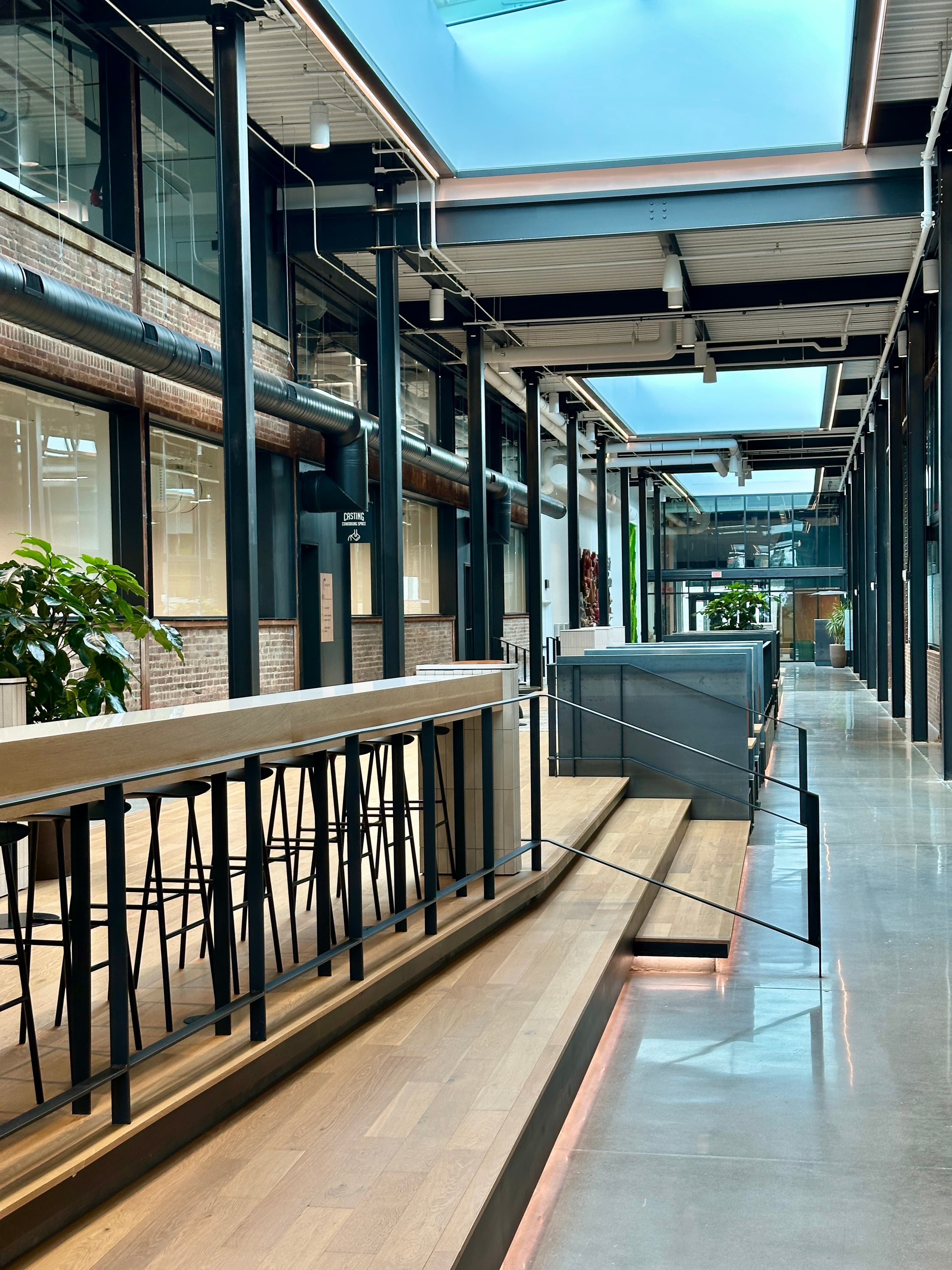 Modern industrial office interior with skylights, wooden bar seating, and black metal structural beams.